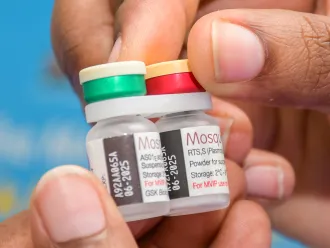 A close up shot of a hand holding two vials of the malaria vaccine
