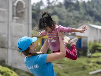 A woman, a UNICEF Staff member, raises a child high above her head, capturing a delightful moment of connection and joy in their interaction.