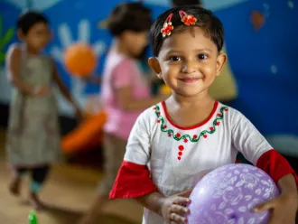 A young girl holds a ball and smiles for a photo. 