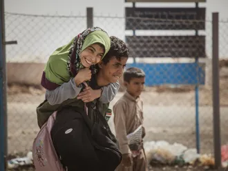 In Yemen, a boy carries a smiling girl wearing a green headscarf on his back. 