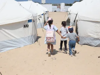Children walk through the tents in the UK-FCDO supported camp in Rafah, southern the Gaza Strip.