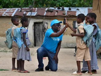 Un employé de l’UNICEF tape dans la main d’un jeune garçon tandis que d’autres enfants se tiennent autour d’eux.