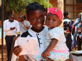A mother holds her child lovingly while also showing the child's birth registration certificate. 