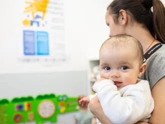 A mother lovingly holds her baby in a warmly lit room, showcasing a tender moment between them.