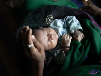 A newborn sleeps in their mother's lap in a HBPNC (Home-based postnatal care) in Balolabadi, Jhabhua, Madhya Pradesh, India. 