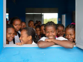 A group of young girls smile and look out from a window.