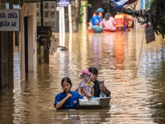  A woman, a man and child navigate a flooded street, showcasing the impact of heavy rainfall on their surroundings.