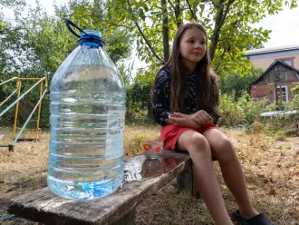 A girl is sitting n a bench next to the bottle of clean water.