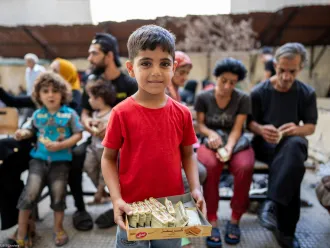 A boy in red shirt stands in front of people sitting together in Lebanon