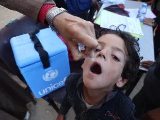 A child is being vaccinated while UNICEF's vaccination cold storage can been seen as well