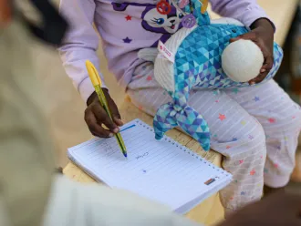 Assourita*, a 5-year-old girl scribbles on a notepad. 