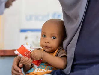 A child sits in their mother's lap as they hold a packet of RUTF in Sudan