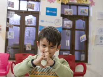A child makes heart shape with their hands at a child protection centre in Syria 
