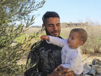 Mohamed, Morei’s father, holds his one-year-old son in the yard of their home in Obada village, Rural Damascus, Syria.