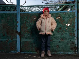A Ukrainian child, looks towards the camera while wearing a winter jacket and red tuque.