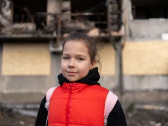 Eight-year-old Myroslava stands in front of a bombed-out residential building, one of several damaged in a missile strike on 7 March in Eastern Ukraine.