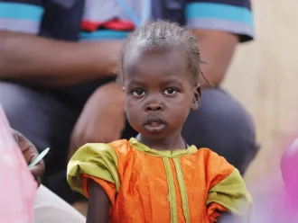 A child looks on as health workers screen children for malnutrition at a UNICEF-supported Primary Health Clinic in Tawila, North Darfur, Sudan