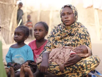Amani carries her newborn baby next to her makeshift shelter in Tawila where she fled with her family after intensified fighting back home in Al Fasher, North Darfur.