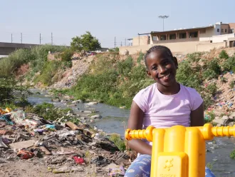 Le 16 septembre 2025 : Ompfuna, dix ans, roule en trottinette le long de la rivière polluée de Jukskei à Johannesburg, en Afrique du Sud.