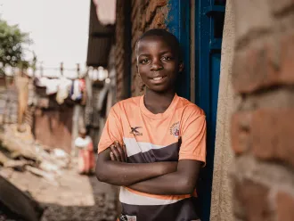 Boy with arms crossed standing in a doorway in a residential alley.