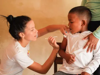 A healthcare worker administers a vaccine to a young boy sitting calmly, with an adult’s supportive hand on his shoulder. 