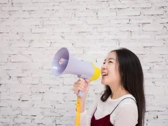 Smiling teen girl holding megaphone in front of a white brick wall