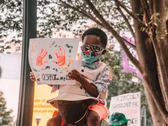 A child sits on a man's shoulders holding a protest sign.