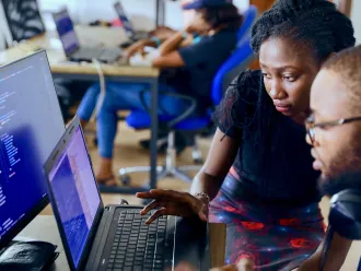 a man and a woman work at a computer which is showing code.