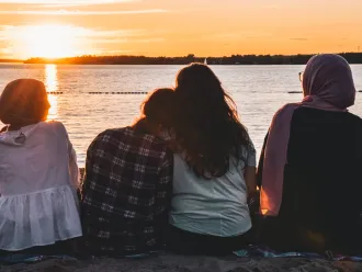 A group of young girls sit facing a sunset.