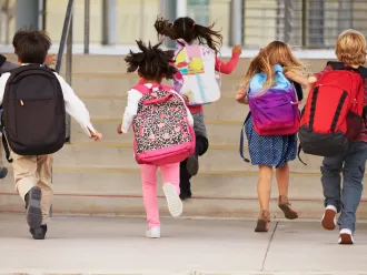 Kids wearing backpacks running into school