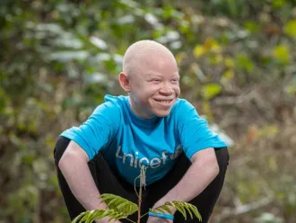 Emmanuel, a young climate advocate, plants a tree while wearing a blue UNICEF t-shirt.